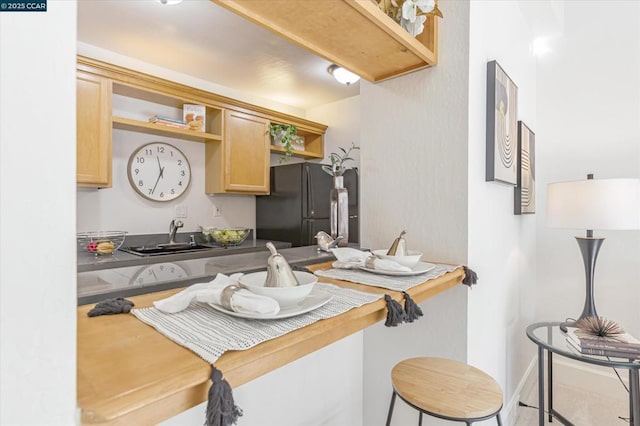 kitchen with black refrigerator, light brown cabinets, a kitchen breakfast bar, and sink