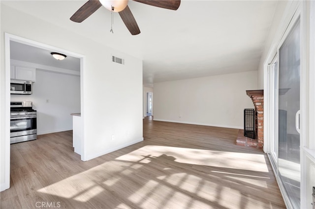 unfurnished living room with ceiling fan, a brick fireplace, and light wood-type flooring