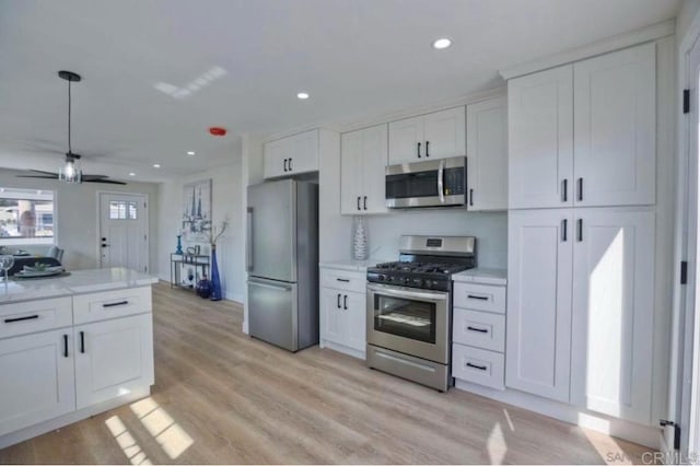 kitchen featuring white cabinets, light wood-type flooring, hanging light fixtures, and stainless steel appliances