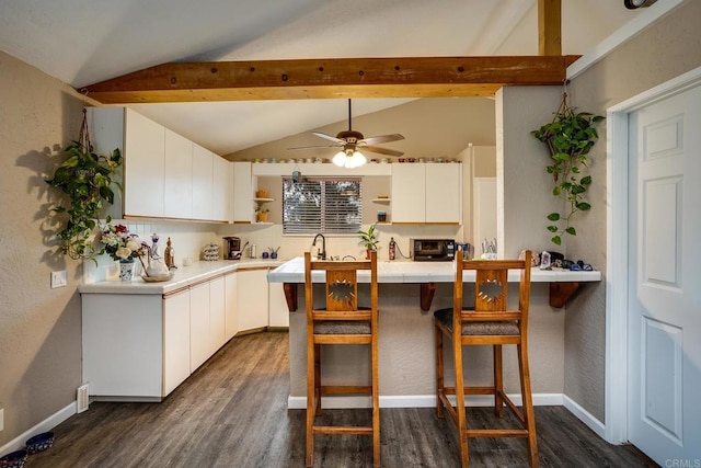 kitchen featuring white cabinets, dark hardwood / wood-style flooring, lofted ceiling with beams, ceiling fan, and a breakfast bar