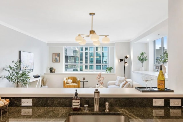 living room featuring sink, ornamental molding, plenty of natural light, and an inviting chandelier