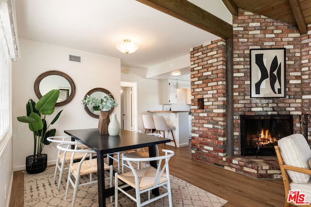 dining area with hardwood / wood-style flooring, a brick fireplace, and vaulted ceiling with beams