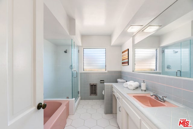 bathroom featuring plus walk in shower, tile walls, heating unit, tile patterned floors, and vanity