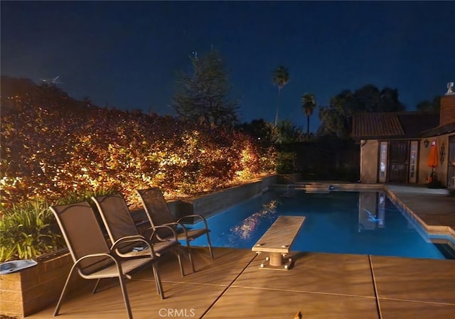 pool at twilight featuring a diving board and a patio