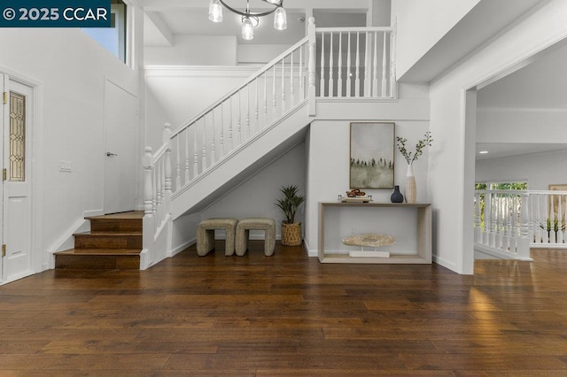 stairway with wood-type flooring, a towering ceiling, and a notable chandelier