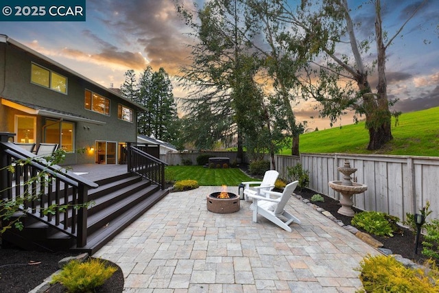 patio terrace at dusk with a wooden deck, a fire pit, and a lawn