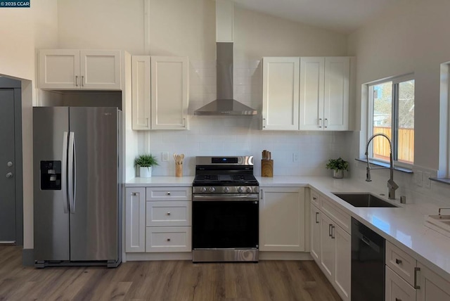 kitchen featuring vaulted ceiling, appliances with stainless steel finishes, white cabinetry, sink, and wall chimney exhaust hood