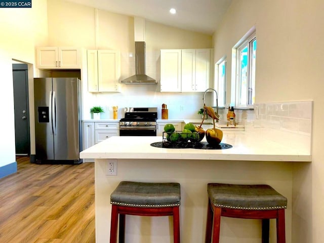 kitchen featuring white cabinetry, stainless steel appliances, a breakfast bar area, and wall chimney range hood