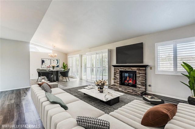 living room with a notable chandelier, a fireplace, lofted ceiling, wood finished floors, and baseboards