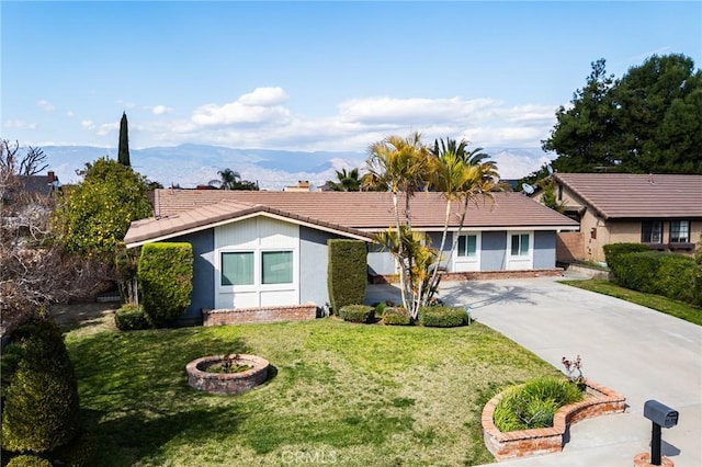 single story home with concrete driveway, a tiled roof, a front yard, a mountain view, and stucco siding