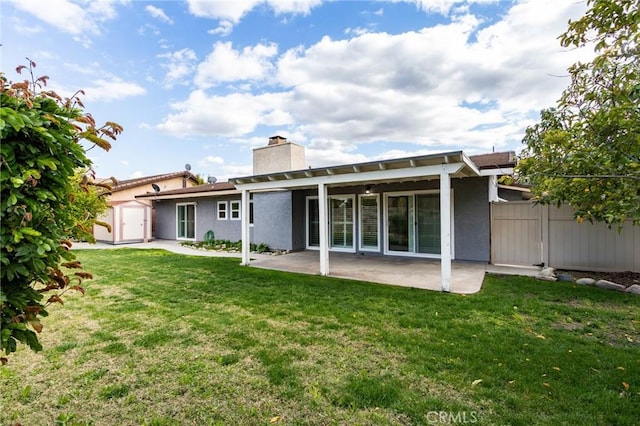 rear view of property featuring a lawn, a chimney, fence, a patio area, and stucco siding