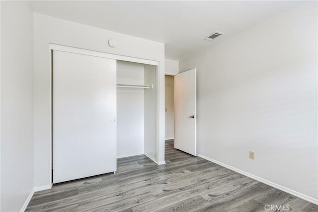 unfurnished bedroom with baseboards, a closet, visible vents, and wood finished floors