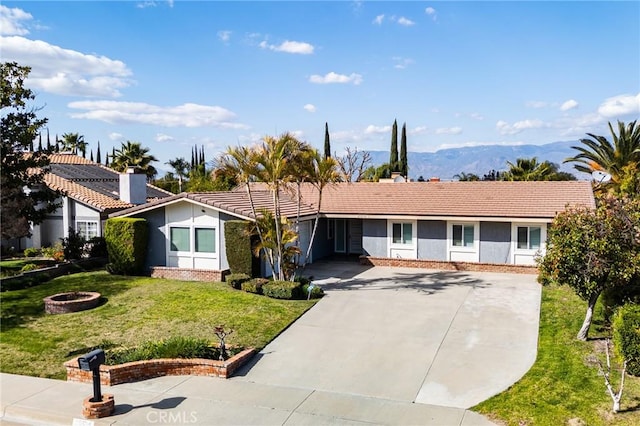 single story home featuring concrete driveway, a front yard, an outdoor fire pit, a mountain view, and a tiled roof