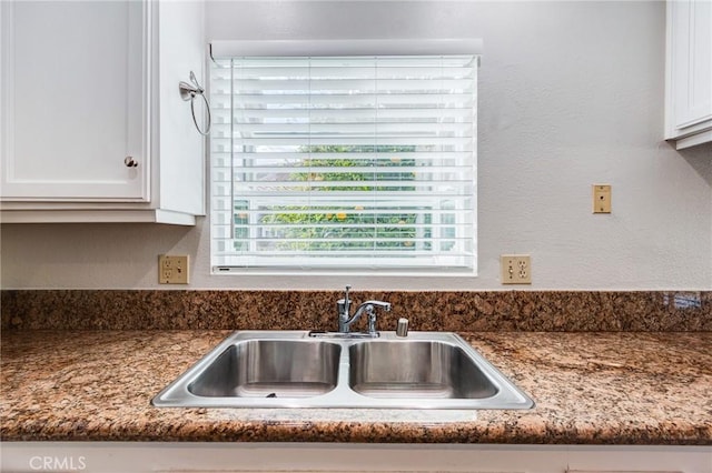 details featuring a textured wall, white cabinetry, a sink, and dark stone countertops