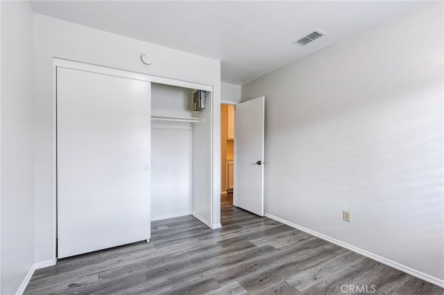 unfurnished bedroom with a closet, visible vents, baseboards, and wood finished floors