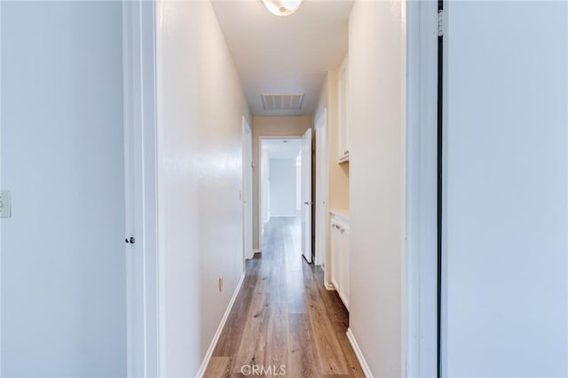 corridor featuring light wood finished floors, baseboards, and visible vents