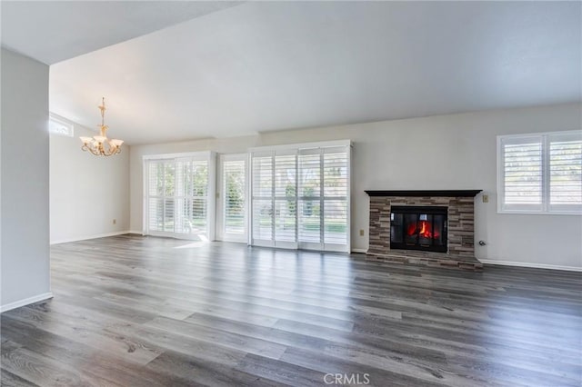 unfurnished living room with wood finished floors, plenty of natural light, a fireplace, and a notable chandelier