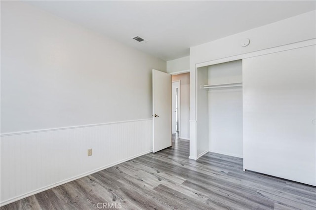 unfurnished bedroom featuring a wainscoted wall, a closet, wood finished floors, and visible vents