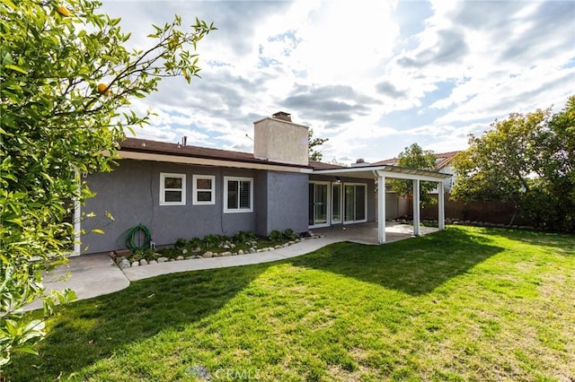 rear view of house with a patio, a yard, fence, and stucco siding