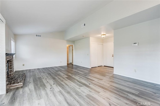 unfurnished living room with vaulted ceiling, a brick fireplace, wood finished floors, and visible vents