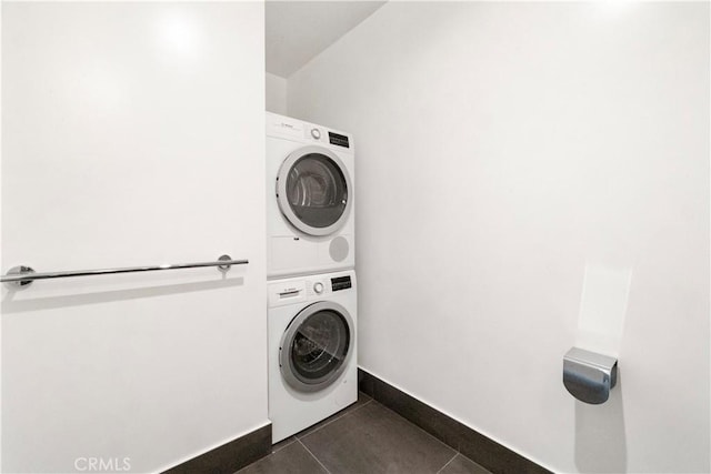 washroom with stacked washer and dryer and dark tile patterned floors