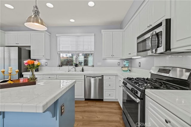 kitchen with sink, appliances with stainless steel finishes, white cabinetry, hanging light fixtures, and a kitchen island