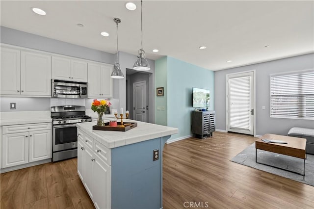 kitchen with a center island, light hardwood / wood-style flooring, pendant lighting, stainless steel appliances, and white cabinets