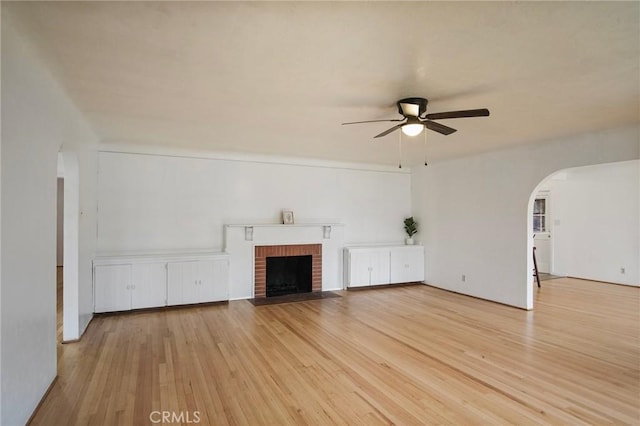 unfurnished living room with light wood-type flooring, ceiling fan, and a brick fireplace