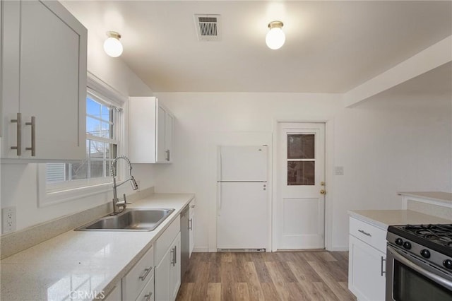 kitchen with light stone countertops, white cabinets, stainless steel appliances, sink, and light wood-type flooring