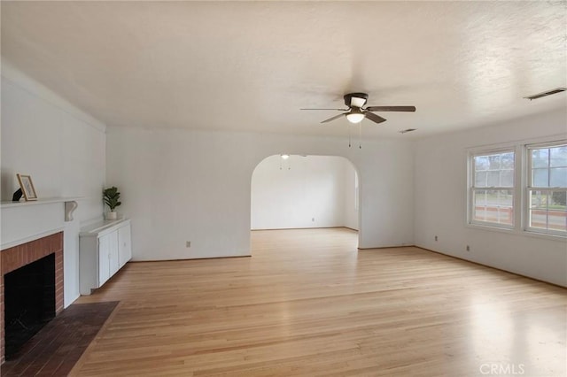 unfurnished living room featuring ceiling fan, a brick fireplace, and light hardwood / wood-style floors