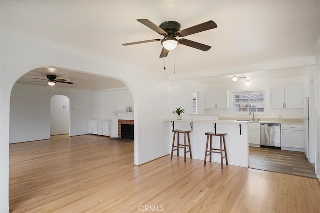 kitchen featuring kitchen peninsula, light hardwood / wood-style flooring, dishwasher, white cabinetry, and a kitchen bar