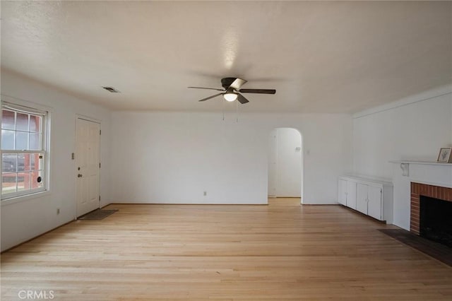 unfurnished living room with ceiling fan, a brick fireplace, and light hardwood / wood-style flooring