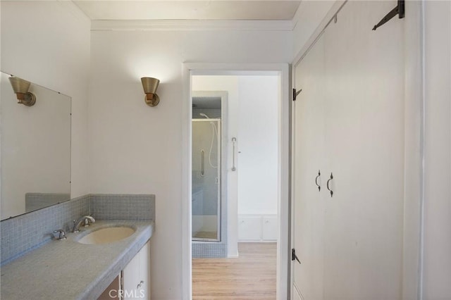 bathroom with wood-type flooring, vanity, decorative backsplash, walk in shower, and ornamental molding