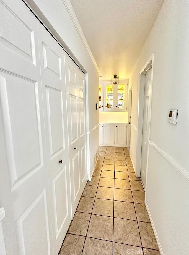 hall featuring light tile patterned floors and crown molding