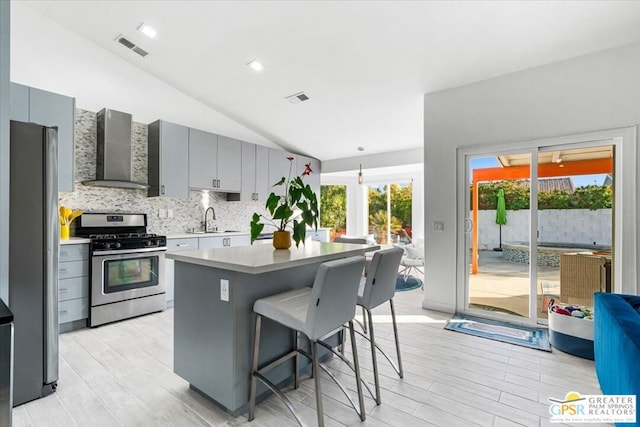 kitchen with vaulted ceiling, wall chimney range hood, sink, stainless steel appliances, and gray cabinets