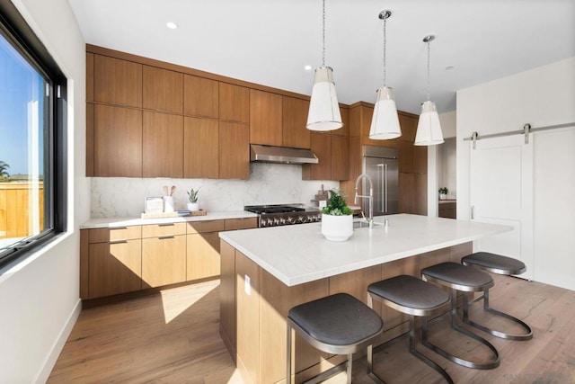 kitchen with built in refrigerator, a center island with sink, light hardwood / wood-style flooring, pendant lighting, and a barn door