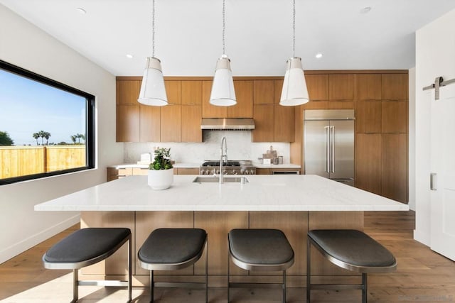 kitchen featuring light hardwood / wood-style flooring, a kitchen island with sink, hanging light fixtures, stainless steel built in refrigerator, and a barn door