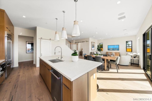 kitchen with sink, hanging light fixtures, stainless steel dishwasher, an island with sink, and a barn door