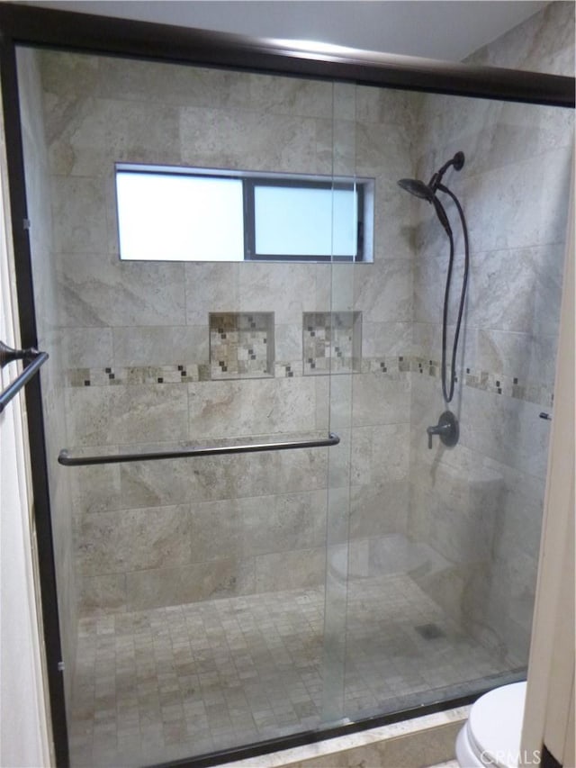 bathroom with a shower with door, toilet, and a wealth of natural light