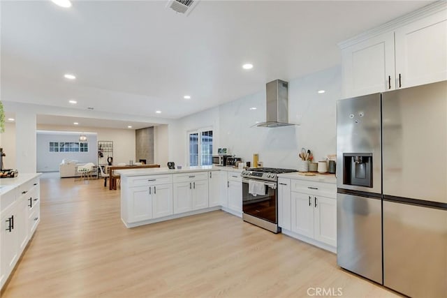 kitchen with kitchen peninsula, appliances with stainless steel finishes, white cabinets, island exhaust hood, and light hardwood / wood-style floors