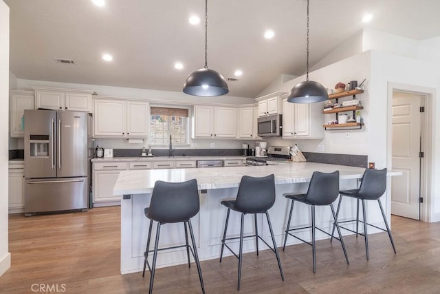 kitchen with a kitchen breakfast bar, white cabinets, appliances with stainless steel finishes, and vaulted ceiling