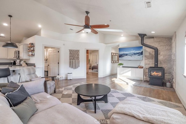 living room with ceiling fan, light hardwood / wood-style flooring, high vaulted ceiling, and a wood stove