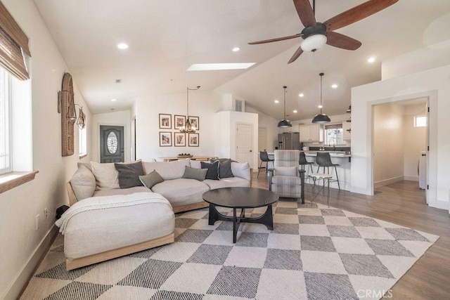 living room featuring vaulted ceiling with skylight, light hardwood / wood-style flooring, and ceiling fan