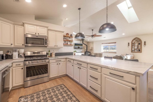 kitchen featuring pendant lighting, appliances with stainless steel finishes, lofted ceiling with skylight, and kitchen peninsula