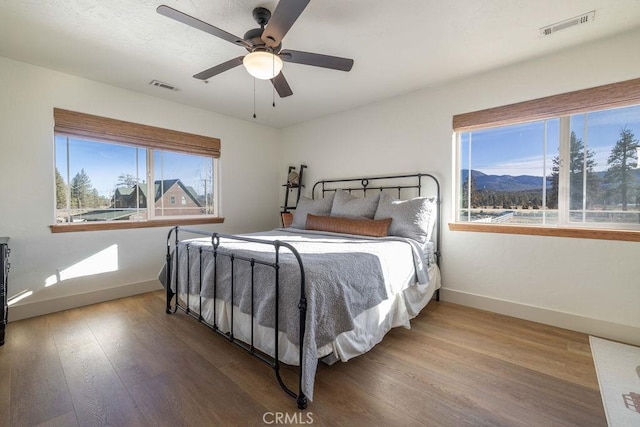 bedroom with a mountain view, ceiling fan, and wood-type flooring