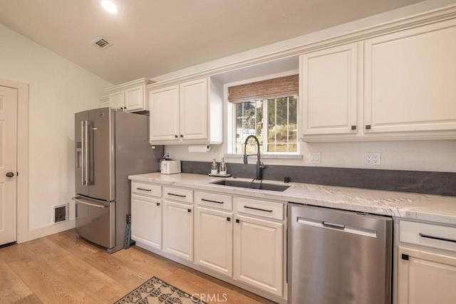 kitchen featuring sink, light wood-type flooring, stainless steel appliances, light stone counters, and lofted ceiling