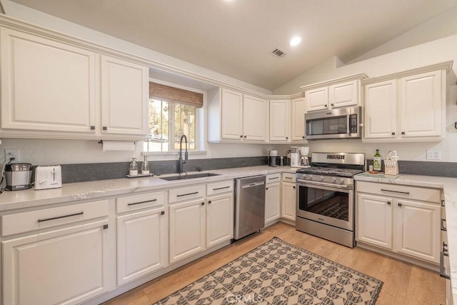 kitchen with vaulted ceiling, appliances with stainless steel finishes, sink, white cabinetry, and light hardwood / wood-style floors