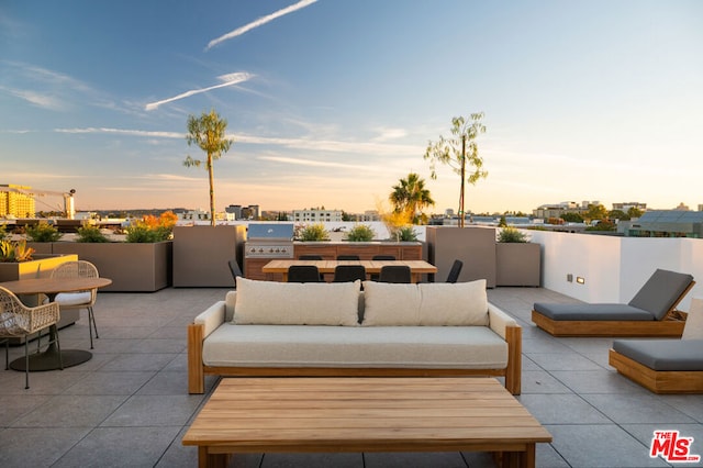 patio terrace at dusk featuring an outdoor kitchen, area for grilling, and an outdoor hangout area