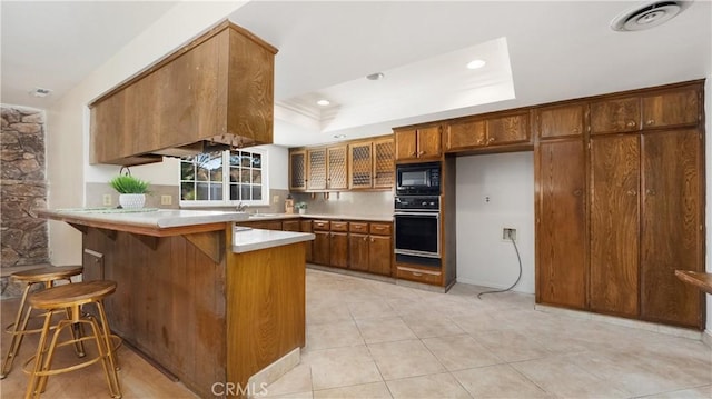 kitchen featuring kitchen peninsula, a raised ceiling, light tile patterned flooring, black appliances, and a breakfast bar area