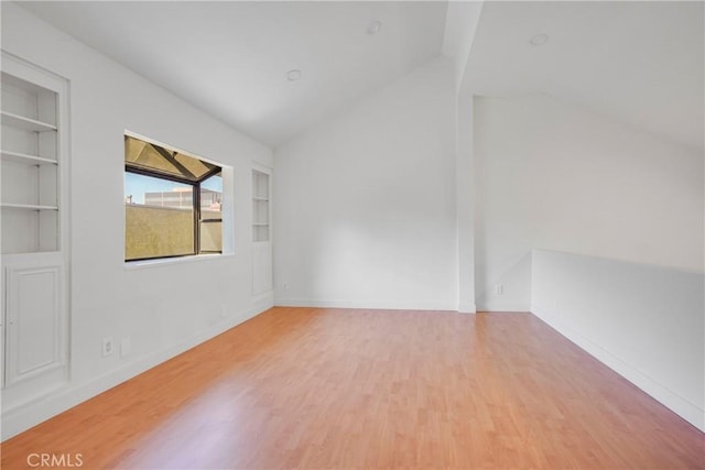 empty room with built in shelves, hardwood / wood-style floors, and lofted ceiling